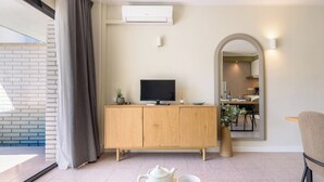 Una sala de estar moderna con un aparador de madera, un televisor de pantalla plana, una mesa de comedor con dos tazas blancas y un espejo grande que refleja un área de comedor.
