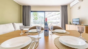 Mesa lista para comer con platos, cubiertos y una botella, con vistas a un edificio y un balcón al fondo.