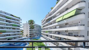 Un hotel de varios pisos con balcones, piscina y una mesa con un bol, vaso y planta.