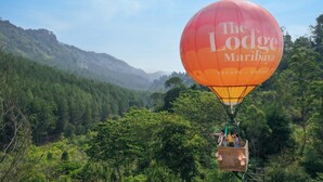 Um balão de ar quente com a marca 'The Lodge Maribaya', suspenso sobre um vale verdejante e florestado.