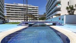 En swimmingpool med fliseterrasse, omgivet af moderne bygninger med altaner.