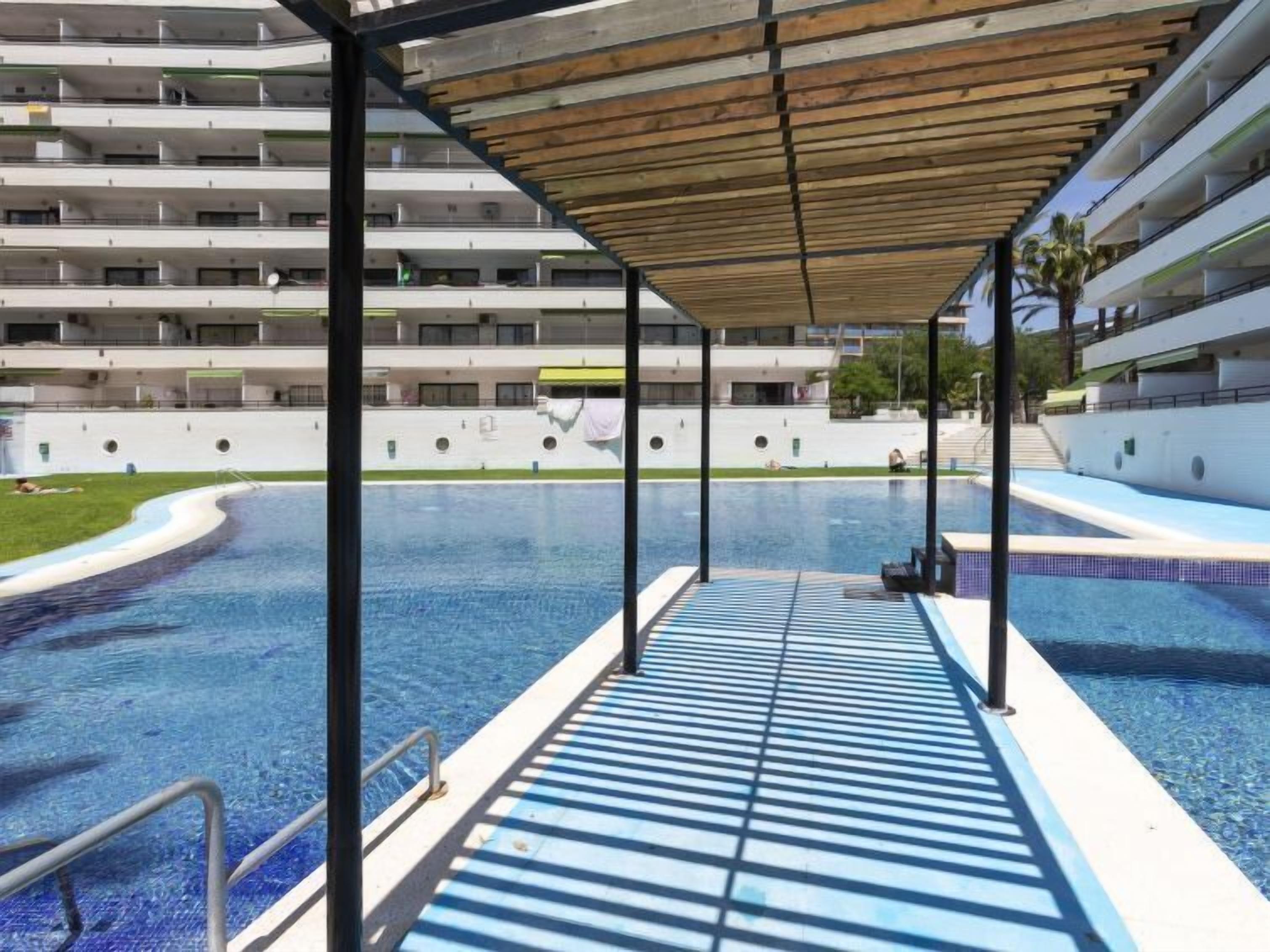 Una piscina con cubierta de madera y vista a un edificio de varios pisos al fondo.