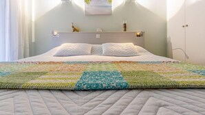 Ein Schlafzimmer mit einem Bett, einem Kopfteil mit Wandleuchten, einer kleinen Ablagefläche mit Dekoration und einem Fenster mit Vorhängen.