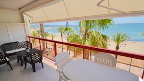 Ein Balkon mit Tisch und Stühlen, der Blick auf einen Strand mit Palmen und das Meer bietet.