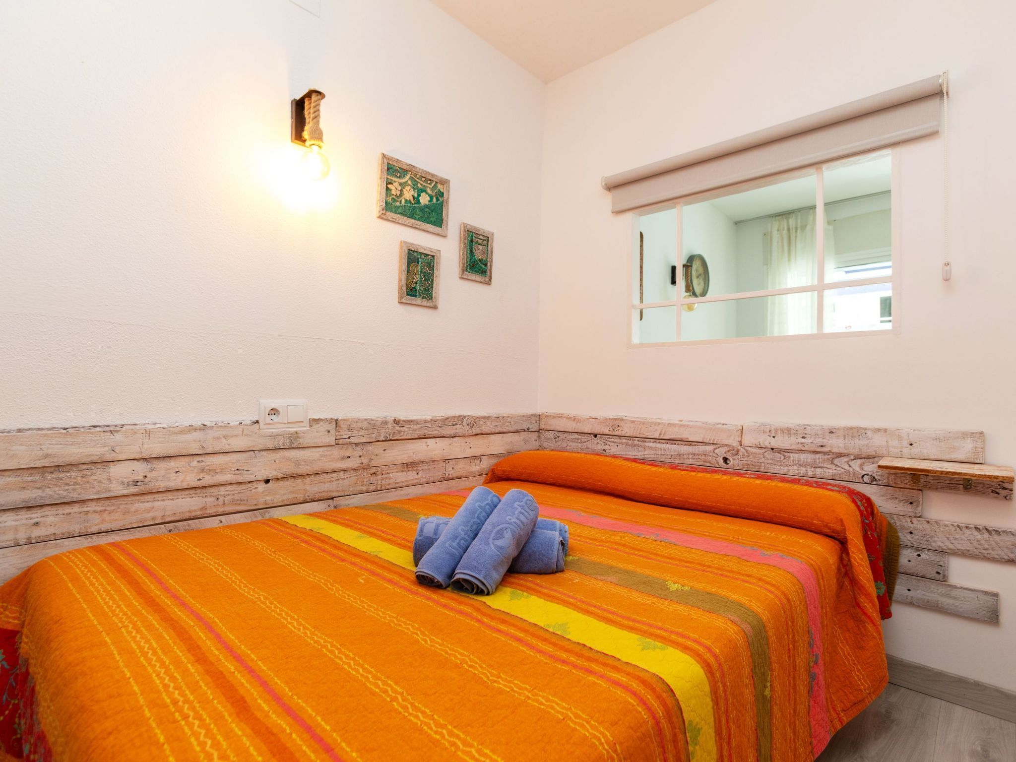 Ein Schlafzimmer mit Holzkopfteil, einem Bett mit gestreifter Bettwäsche, einer Wandleuchte und einem Fenster mit Blick auf eine Uhr.