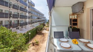 Een balkon met een eettafel gedekt voor twee, met uitzicht op een gebouw met meerdere balkons en een tuin.
