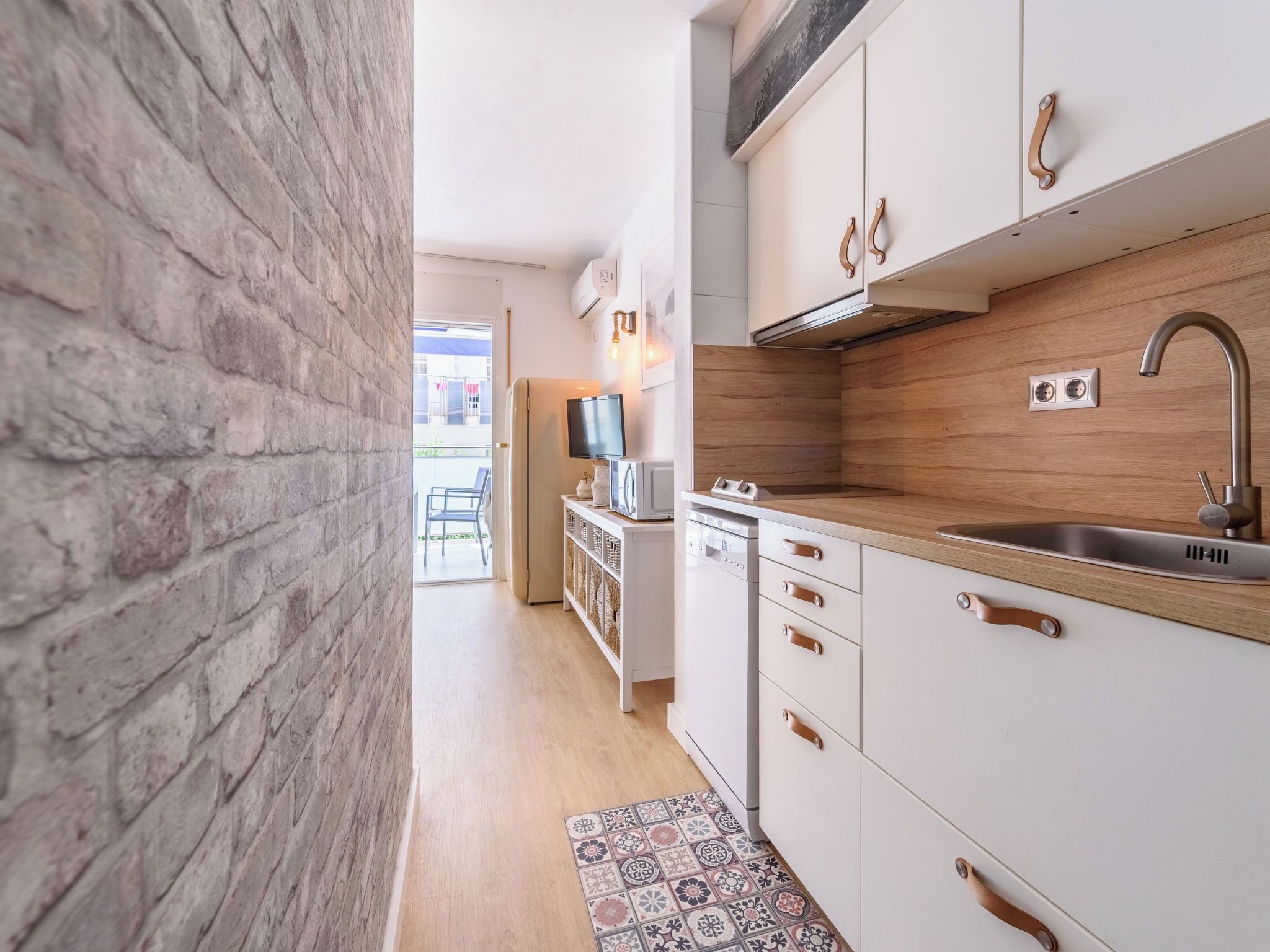 A modern kitchen with white cabinets, a wooden countertop, and a stainless steel sink.
