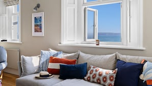 A living room with a sofa, pillows, a hat, and a framed picture on the wall. - Amazing views -  Woodburner - Wi-Fi (Torpoint)