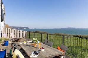 A wooden table with outdoor seating, a view of the sea, and a distant cityscape.