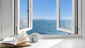 An open window with a view of the sea, a book, and a mug on the windowsill. - Amazing views -  Woodburner - Wi-Fi (Torpoint)
