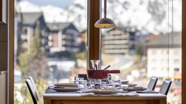 Une table à manger dressée avec des assiettes, des verres et des couverts, avec une vue sur les montagnes en arrière-plan.