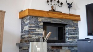 Une cheminée en pierre avec une cheminée en bois, un téléviseur à droite et un chandelier décoratif accroché au mur.