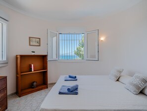 Een slaapkamer met een bed, een houten plank, een raam met uitzicht en een wandlamp.