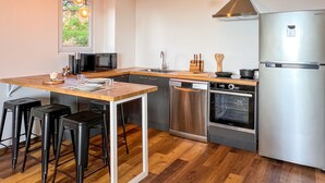 A modern kitchen with a wooden island, stainless steel appliances, and black bar stools. - Manui Swimming Pool Condo with Sea & Moorea views (Puna'auia)