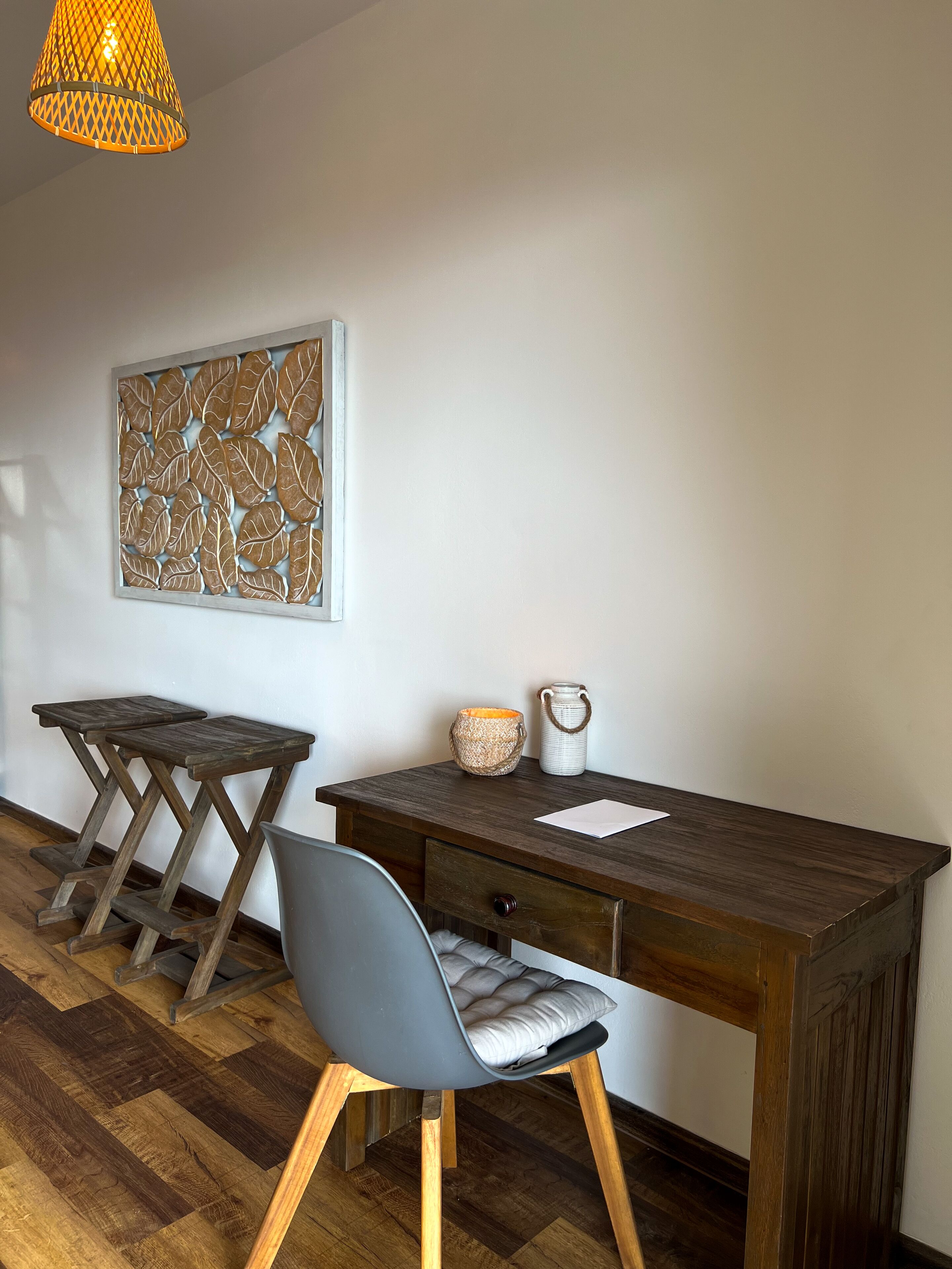 A wooden desk with a chair, a wall art piece, and a hanging light fixture.