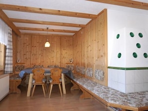 A wooden-paneled room with a long bench, two wooden chairs, and a table.