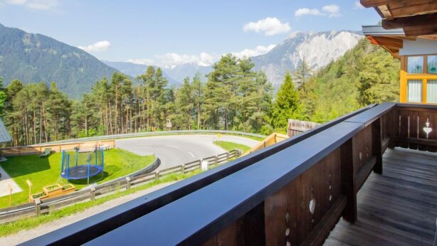 A balcony with a view of a winding road, a trampoline, and a mountain backdrop. - Plattner by Interhome (Ötz)