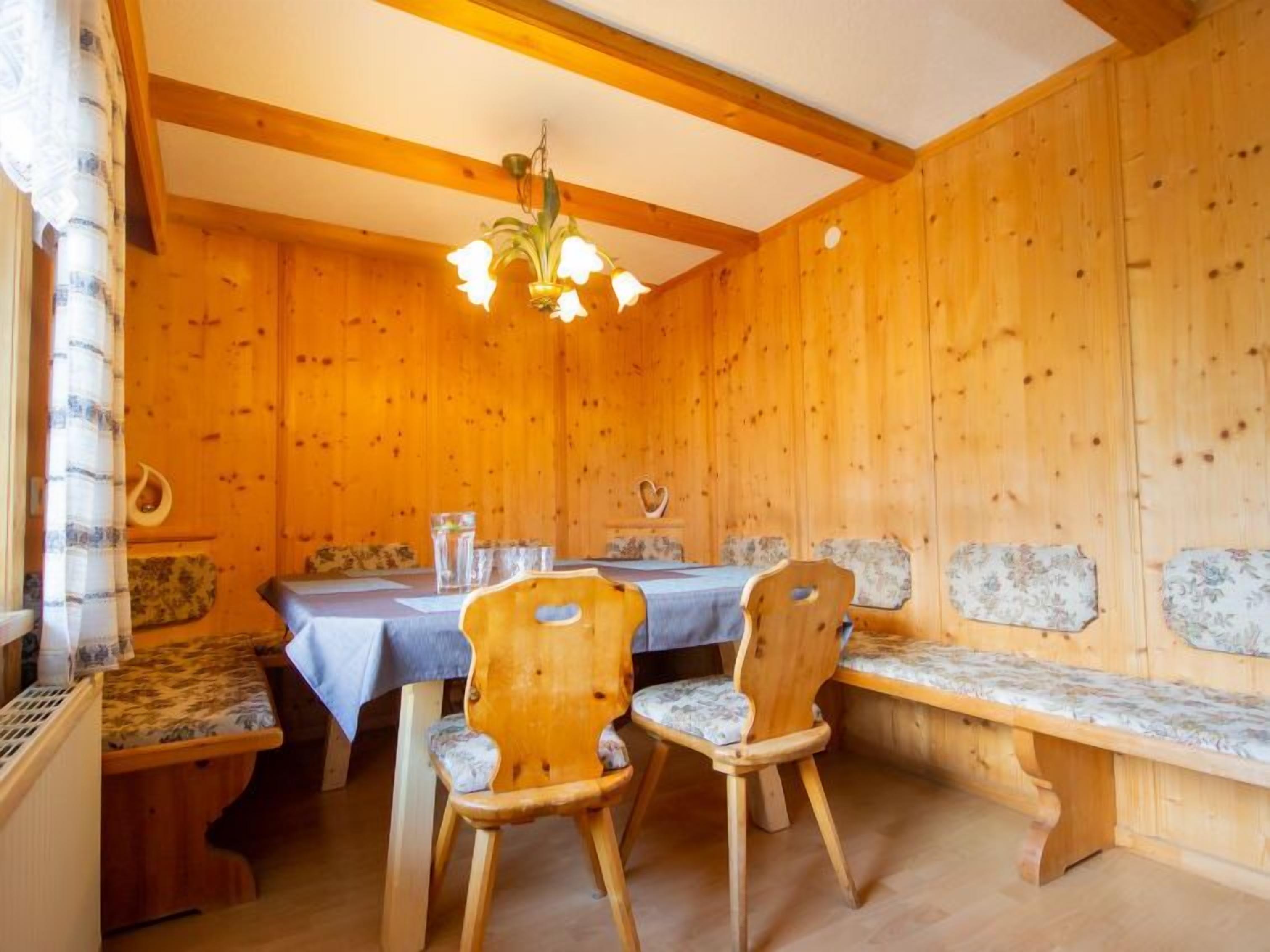Un intérieur en bois comprenant une table à manger, deux chaises, un banc et un lustre.