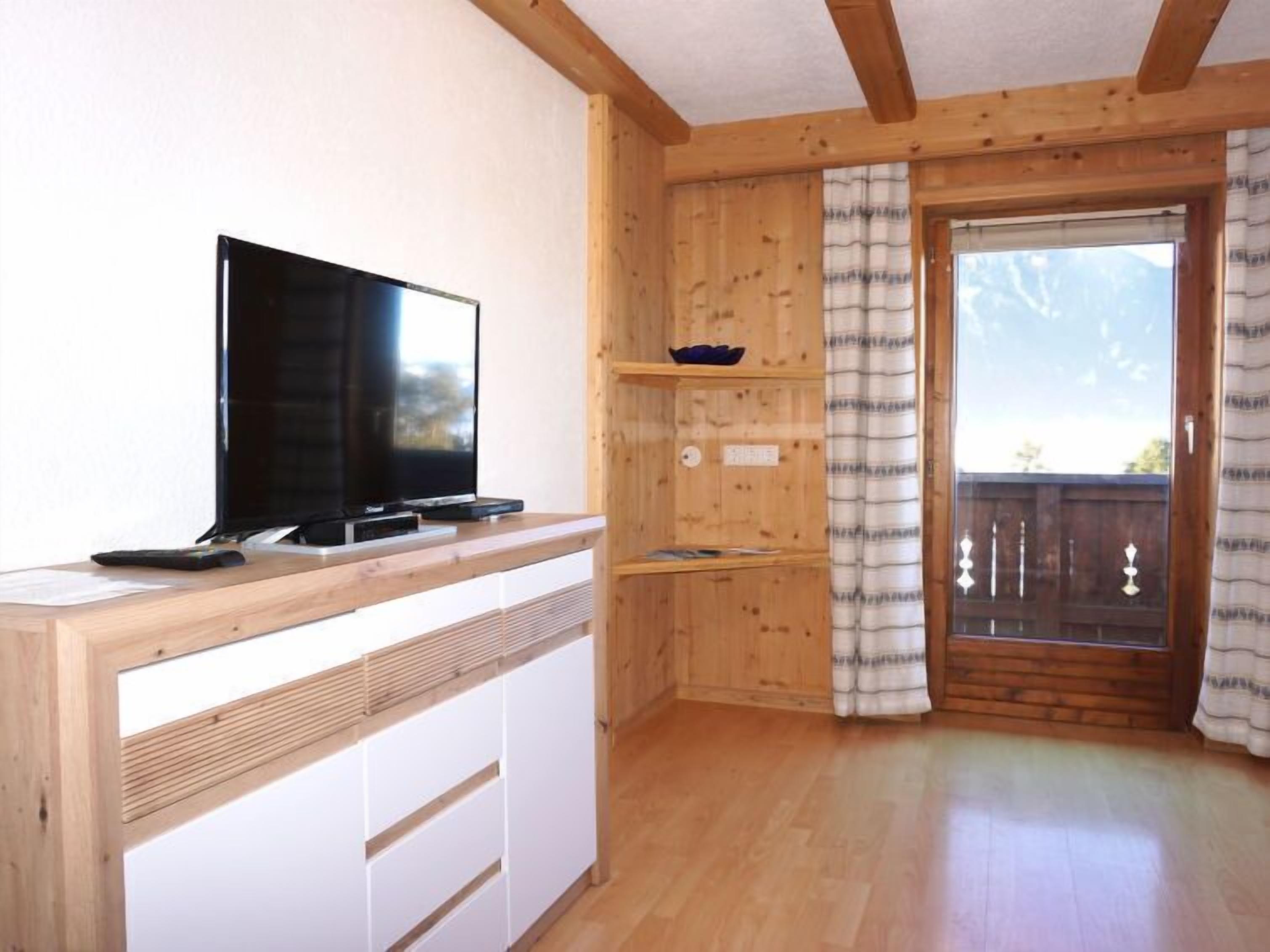 Un intérieur en bois avec un téléviseur posé sur un meuble en bois, une porte coulissante donnant sur une vue dégagée et un plancher en bois.