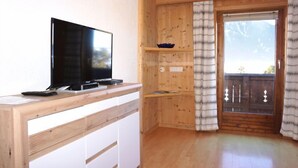 A wooden interior with a TV on a wooden stand, a sliding door with a view, and a wooden floor. - Plattner by Interhome (Ötz)