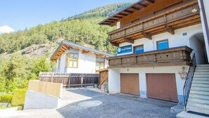 A two-story building with a wooden facade, a sign reading "PLATTHNER," and a view of a forested hillside. - Plattner by Interhome (Ötz)