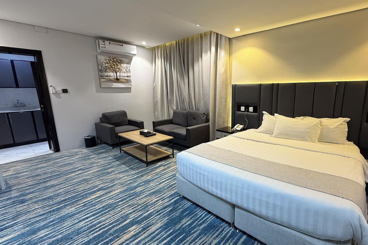 A hotel room with a bed, two armchairs, a coffee table, a desk with a phone, and a painting on the wall.