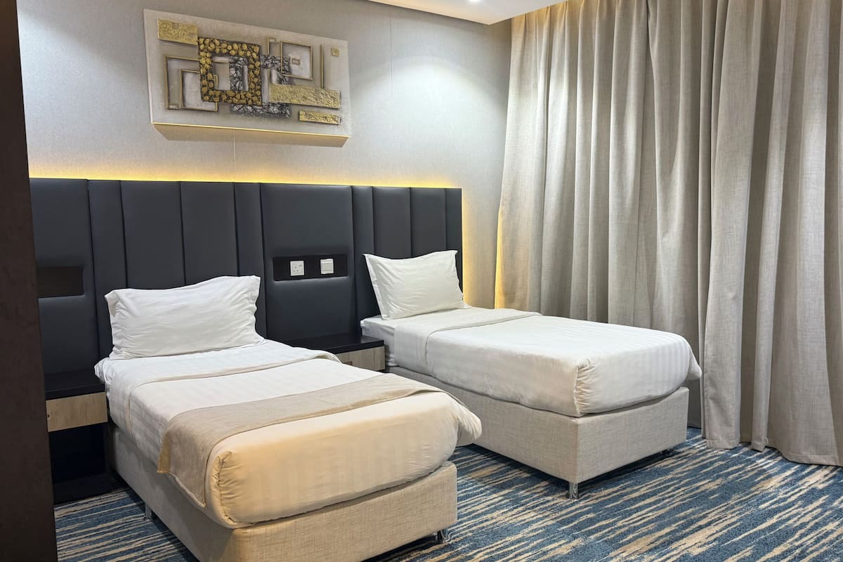 A hotel room with two beds, a headboard, a wall-mounted light fixture, and a large window with curtains.