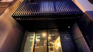 The entrance of a building with a modern design, featuring a glass door and a metal canopy. - AMANECER HOTEL (Tokyo)