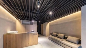 A reception area with a wooden reception desk, a sofa, and a ceiling with linear lighting. - AMANECER HOTEL (Tokyo)