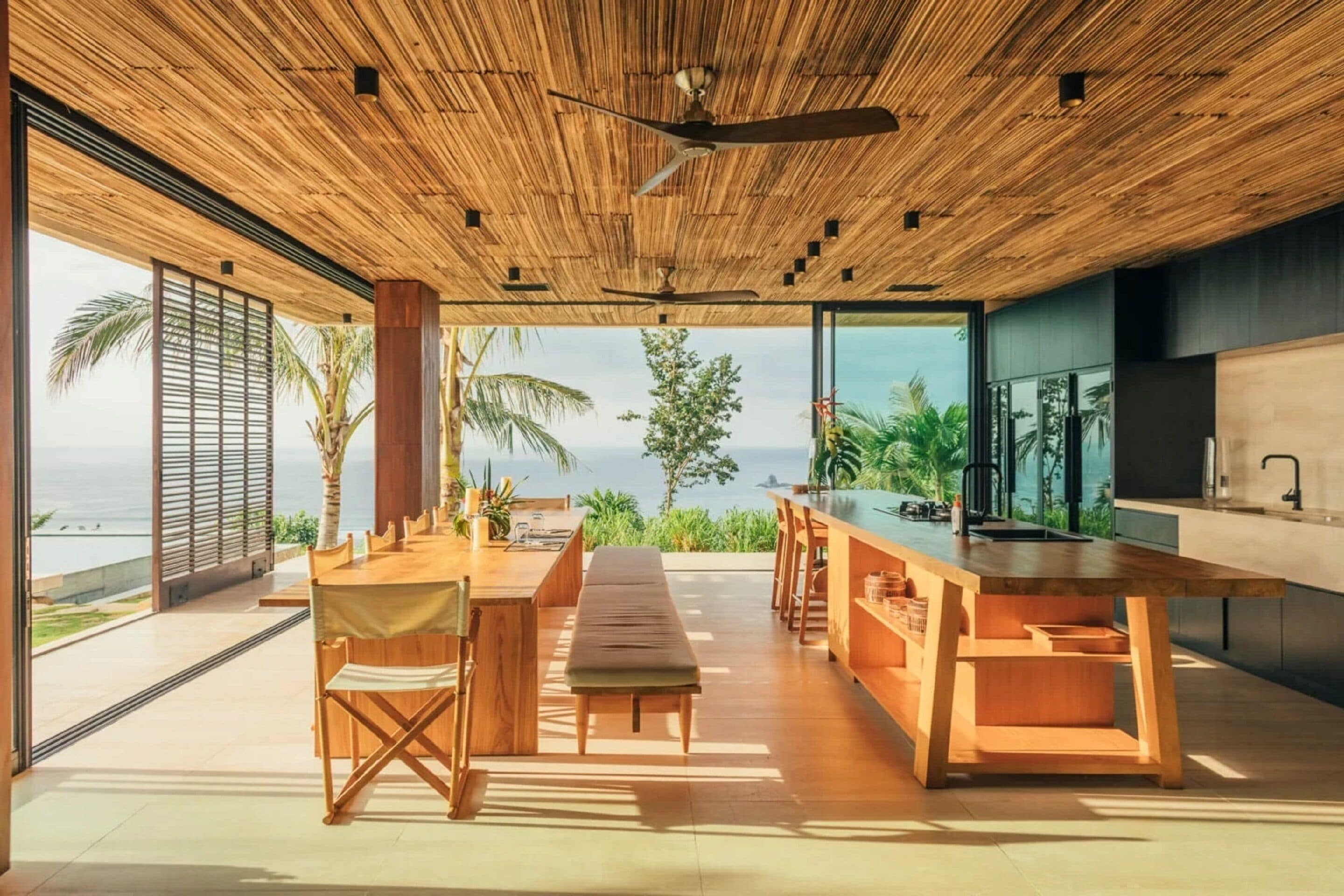 A modern kitchen with a large island, wooden ceiling, and a view of the ocean.