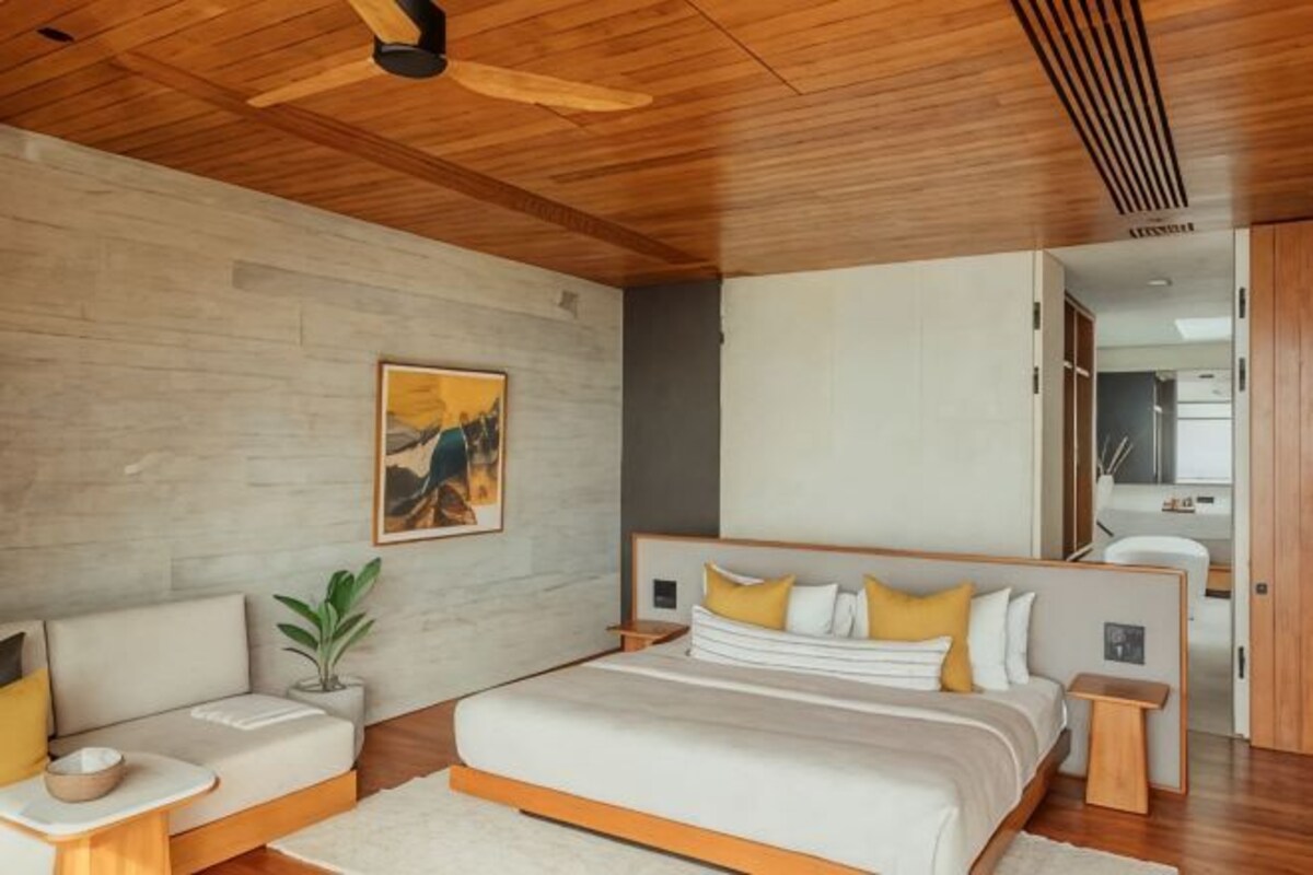 Un dormitorio moderno con una cama grande, mesitas de noche, un ventilador de techo y techo de madera.
