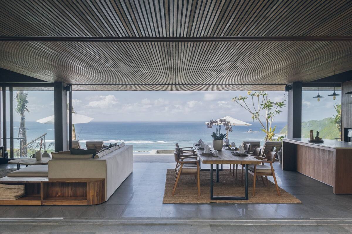 A modern interior with a view of the ocean, featuring a dining area, seating, and a kitchen.