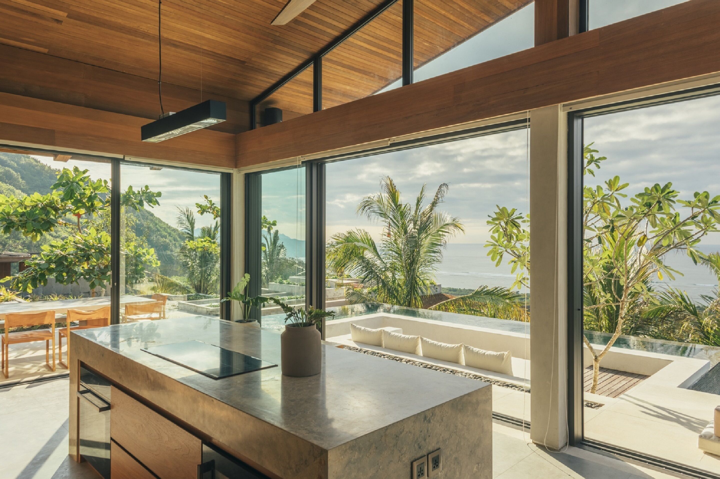 A modern kitchen with large windows, a wooden ceiling, and a view of the ocean and hills.