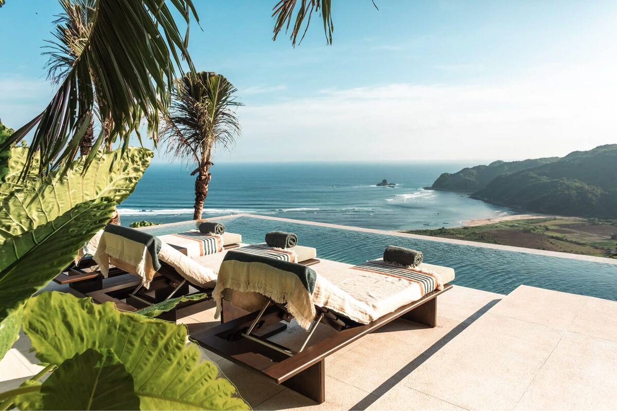 A poolside area with lounge chairs and a view of the ocean.