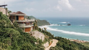 A coastal property with a stone retaining wall, a pathway leading to a beach, and a view of the ocean. - Tampah Hills (Kuta)