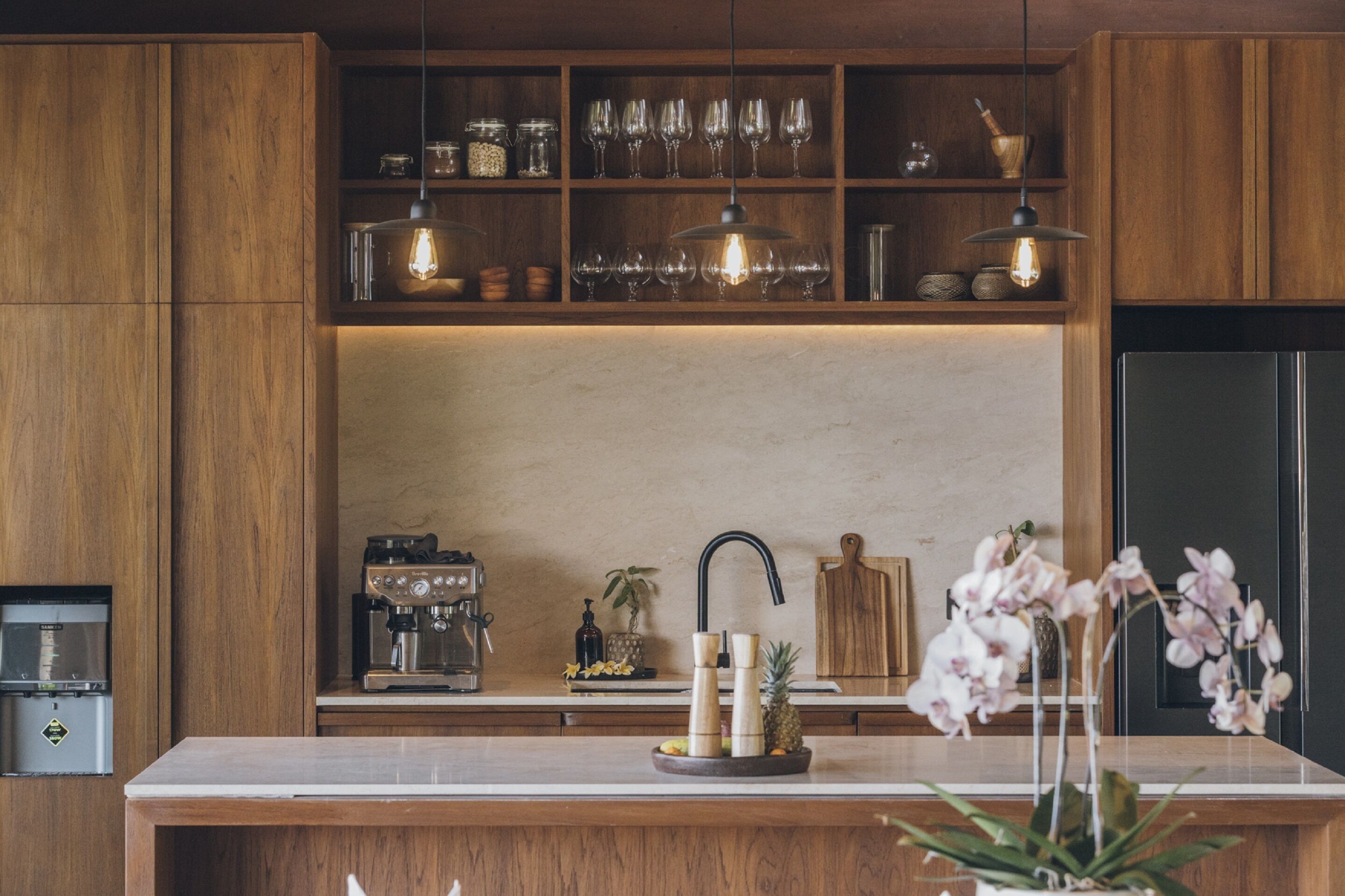 Une cuisine moderne avec des meubles en bois, une machine à café intégrée, un panier de fruits et un évier.