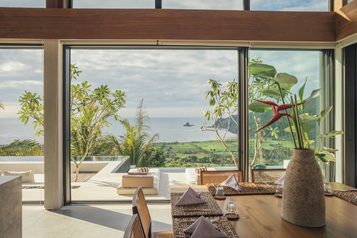 A modern dining area with a view of the ocean and greenery.