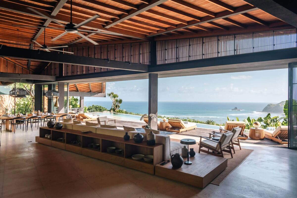 A spacious indoor area with a large window overlooking the ocean, wooden furniture, and a ceiling fan.