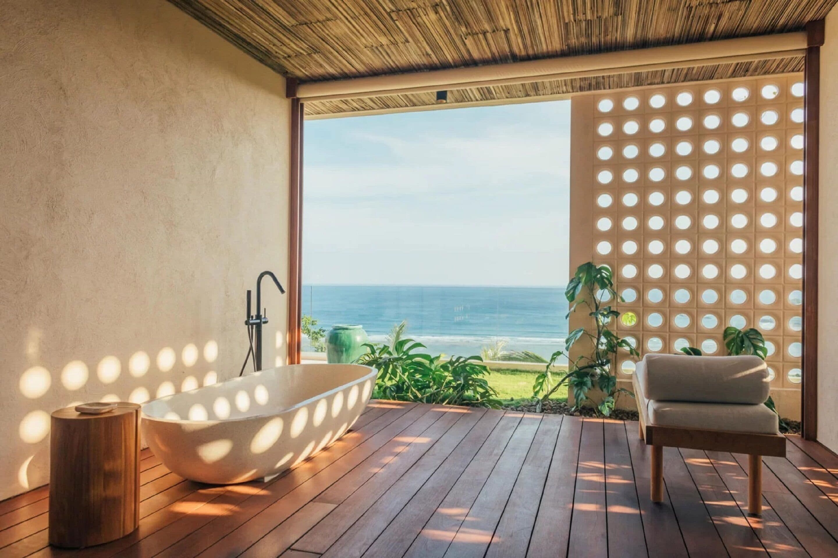 Une salle de bain moderne avec une baignoire sur pieds, un plancher en bois et une vue sur l’océan.