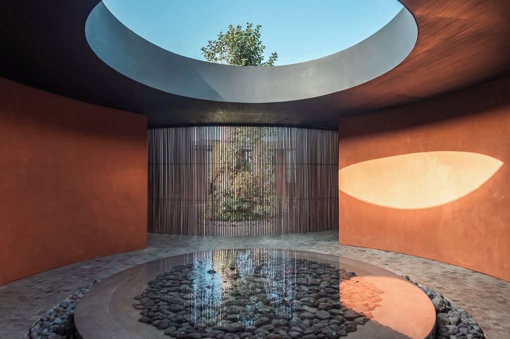 A modern interior with a circular water feature, a sloped ceiling, and a vertical wooden panel.