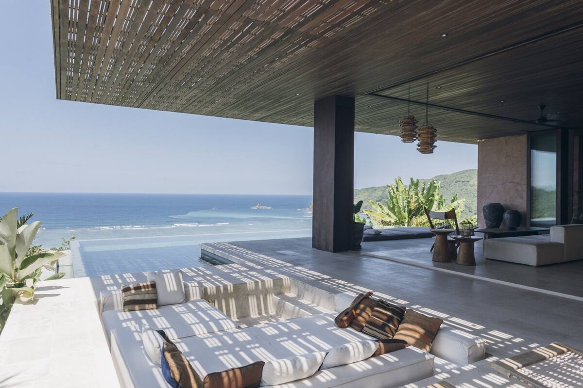 A modern outdoor lounge area with a view of the ocean, featuring a sofa set, a coffee table, and hanging pendant lights.