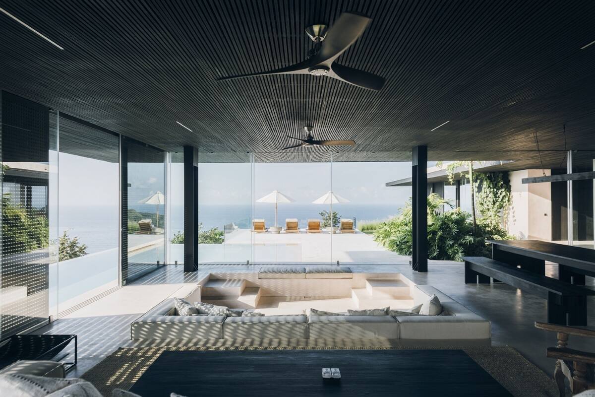 A modern interior with a large seating area, a ceiling fan, and a view of the ocean.