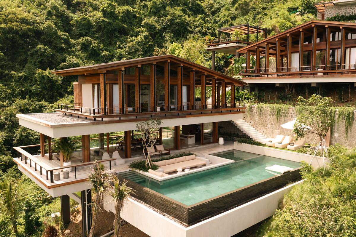 A modern two-story house with a large outdoor pool, wooden deck, and lush greenery.