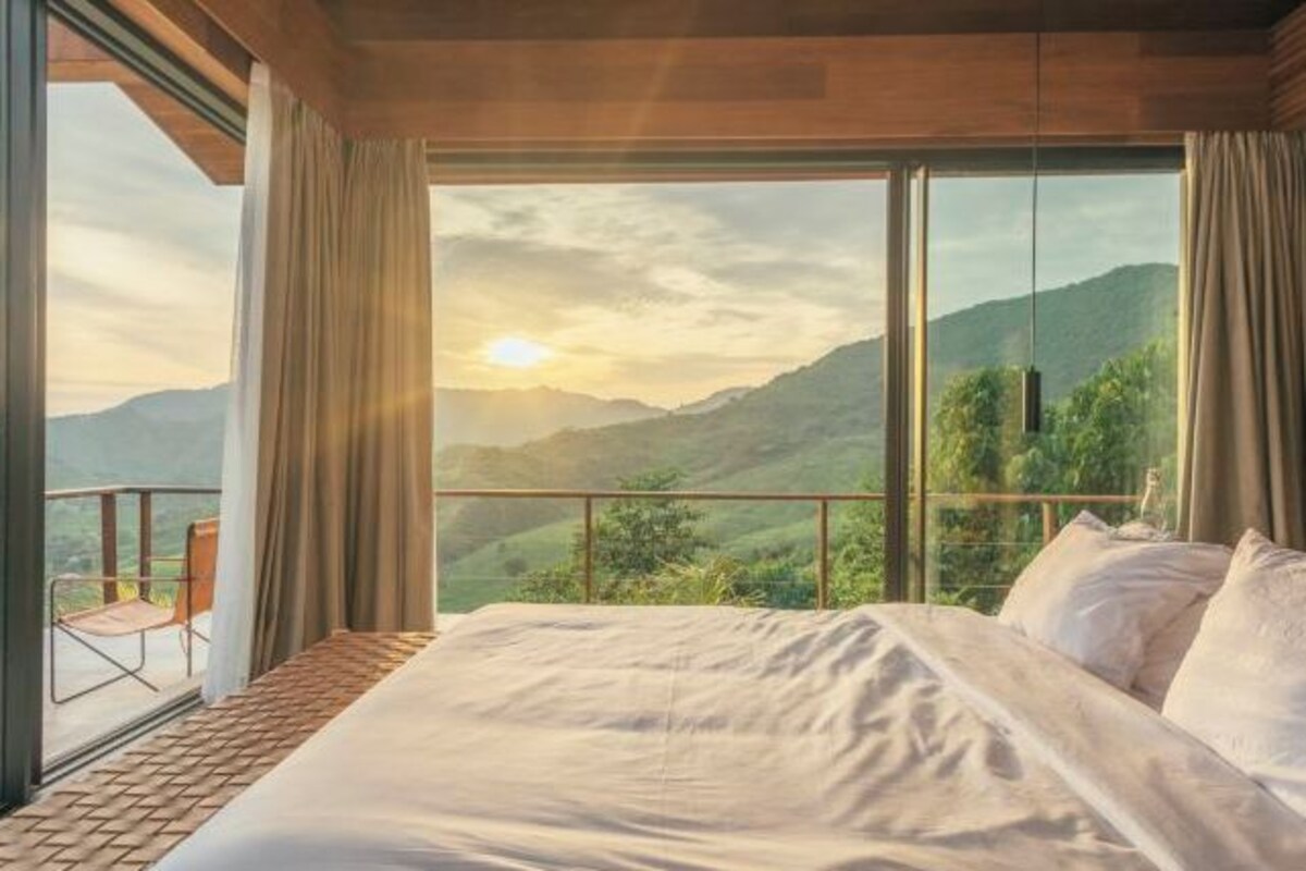 Un dormitorio con una cama grande, vistas a las montañas y un balcón con una silla.