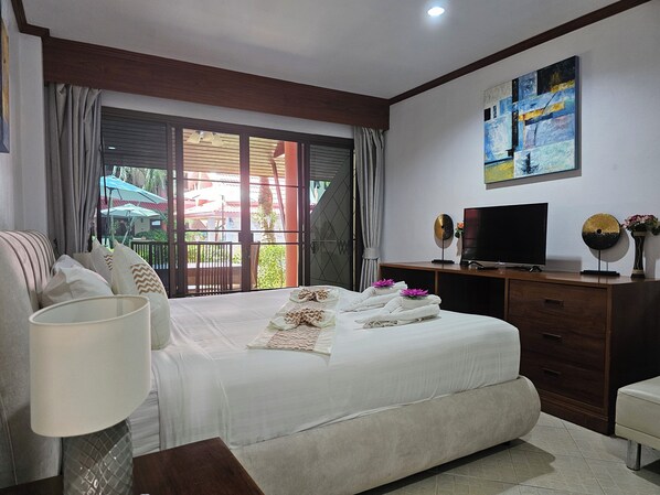 Un dormitorio de hotel con una cama grande, televisión, escritorio y ventana con cortinas.