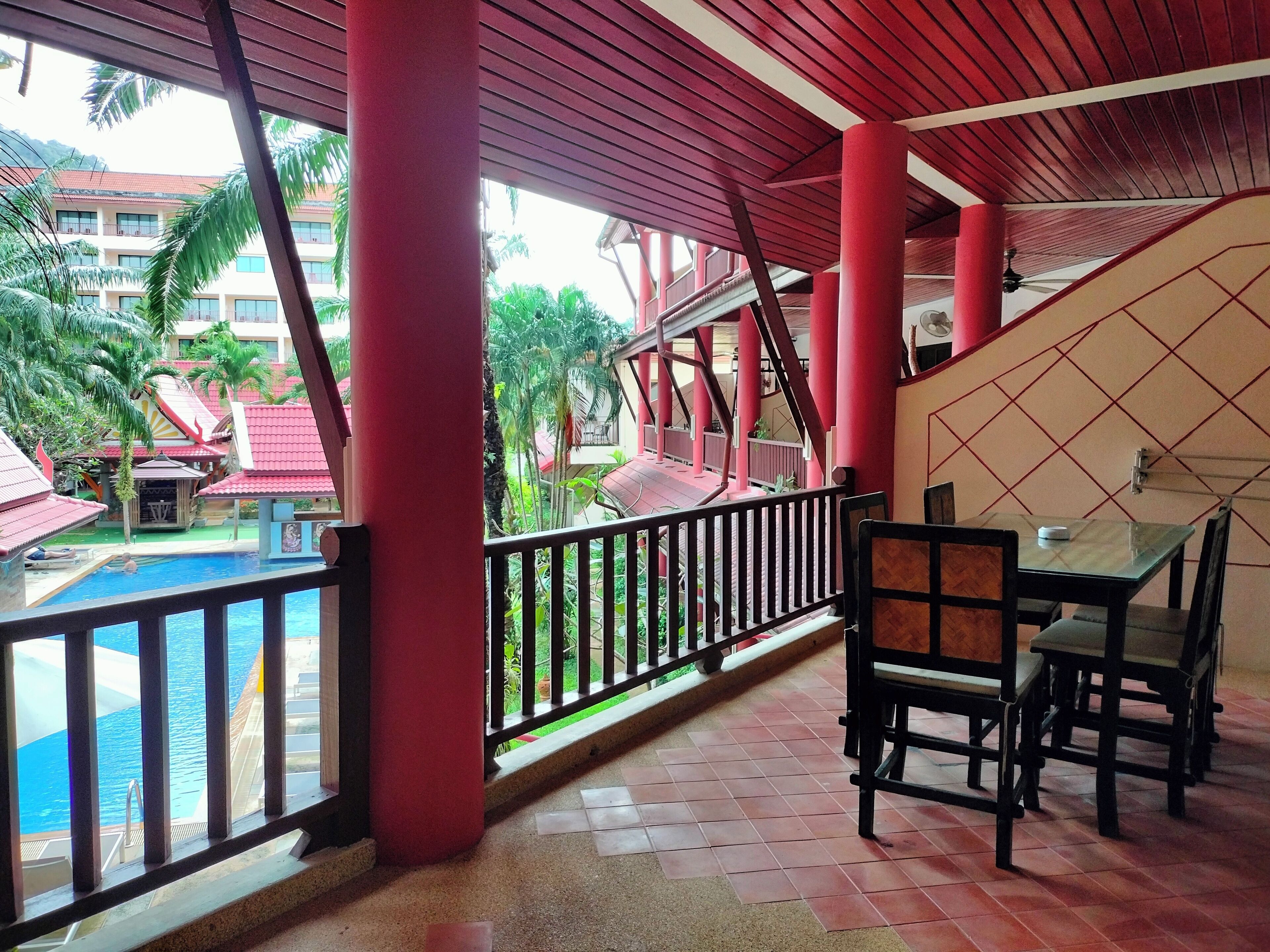 A covered outdoor area with a pool, red pillars, and a dining table with chairs.