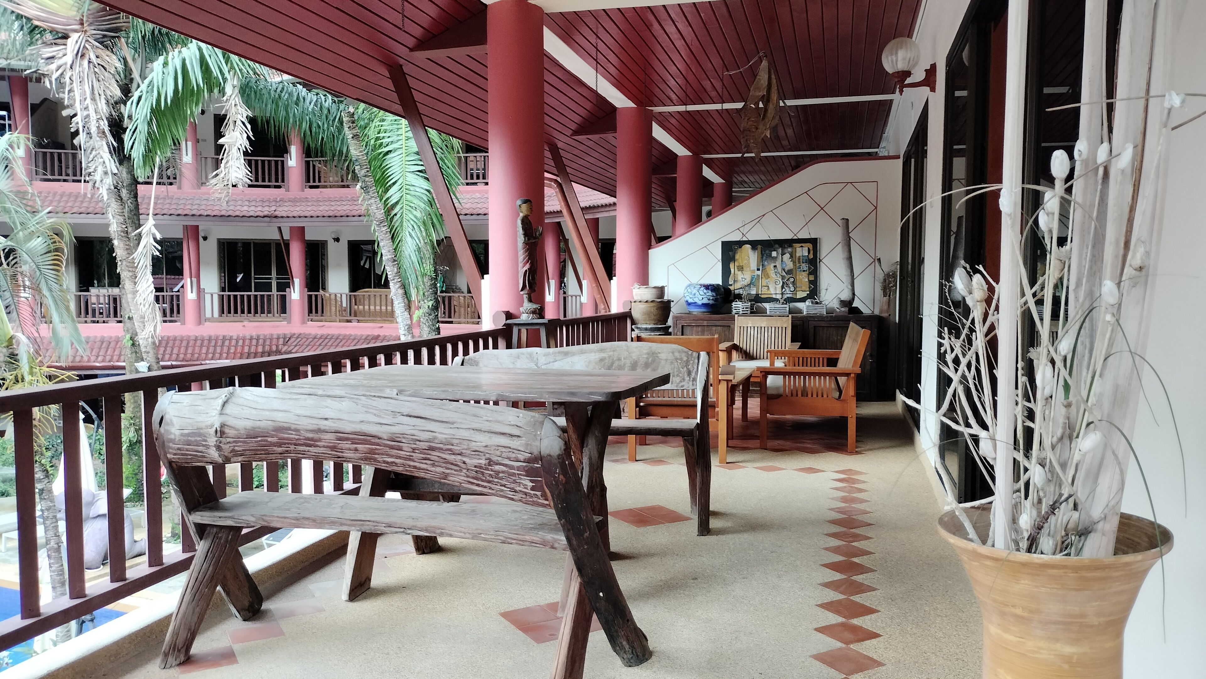Un espacio al aire libre cubierto con una mesa y sillas de madera, una planta en maceta y vista a un edificio con tejado de tejas.