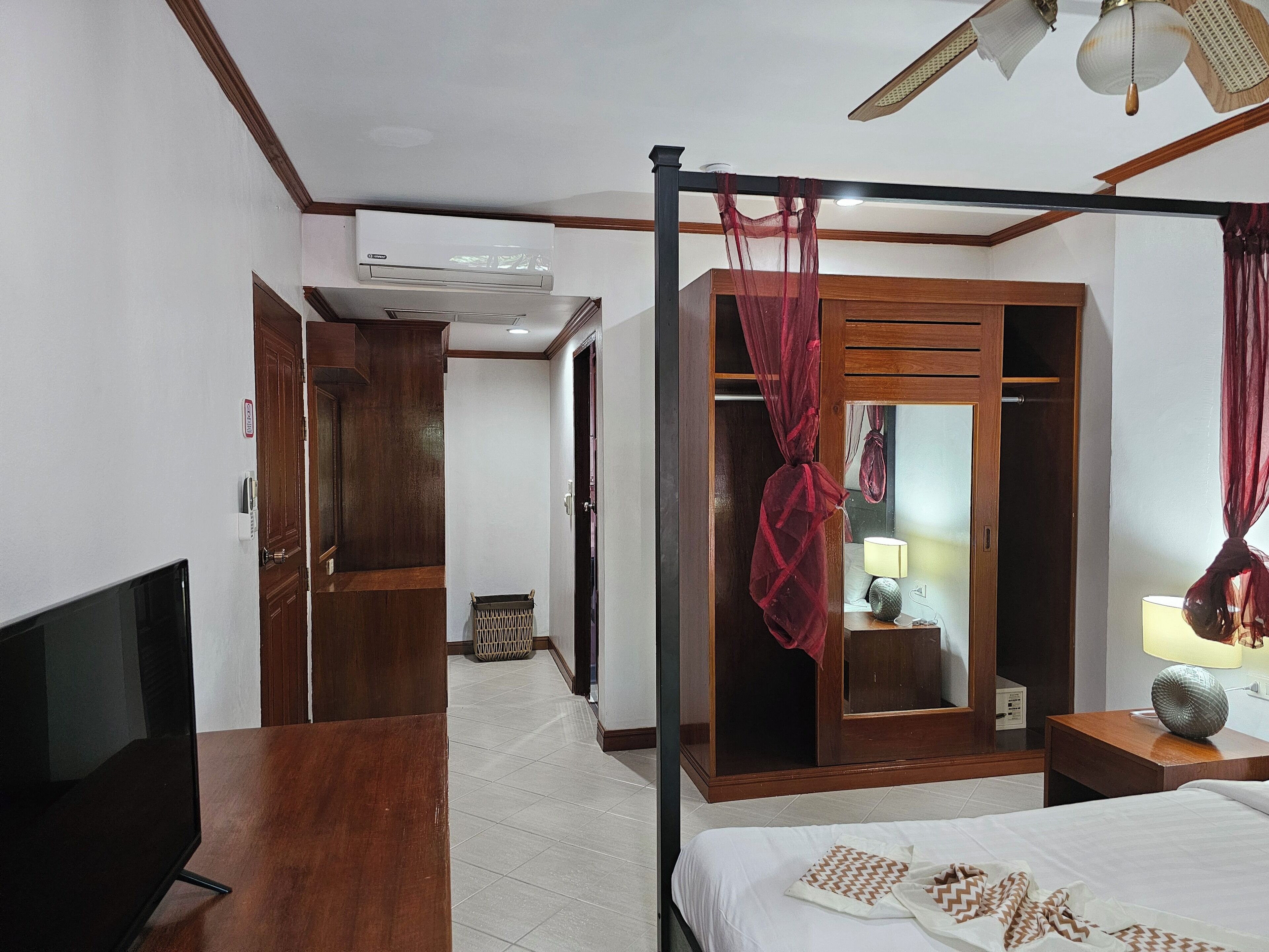A hotel room with a four-poster bed, a television, a wardrobe, a mirror, and a ceiling fan.