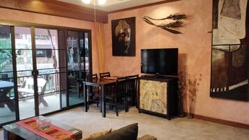 A living room with a dining area, a TV, and a large window overlooking a garden.