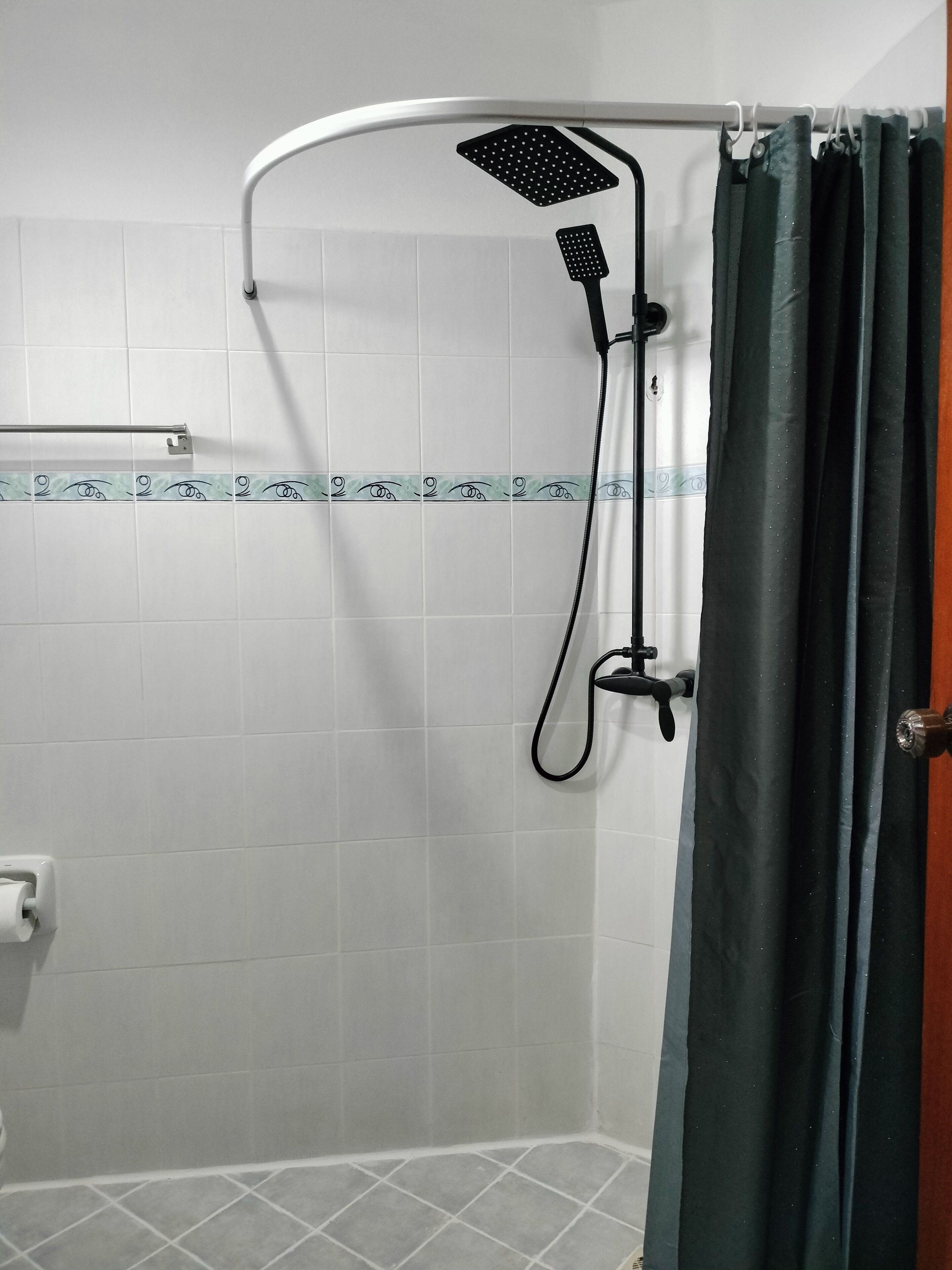 Un espacio de ducha con cabezal de ducha manual, control montado en la pared y cortina.
